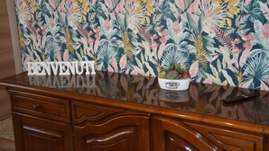 A reception desk with a 'WELCOME' sign, a potted plant, and a tropical leaf-patterned wall. - In the heart of Caprarola cozy apartment within walking distance of all services (Caprarola)