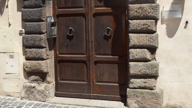 A double wooden door with metal handles, set in a stone wall with a metal decorative element above. - In the heart of Caprarola cozy apartment within walking distance of all services (Caprarola)