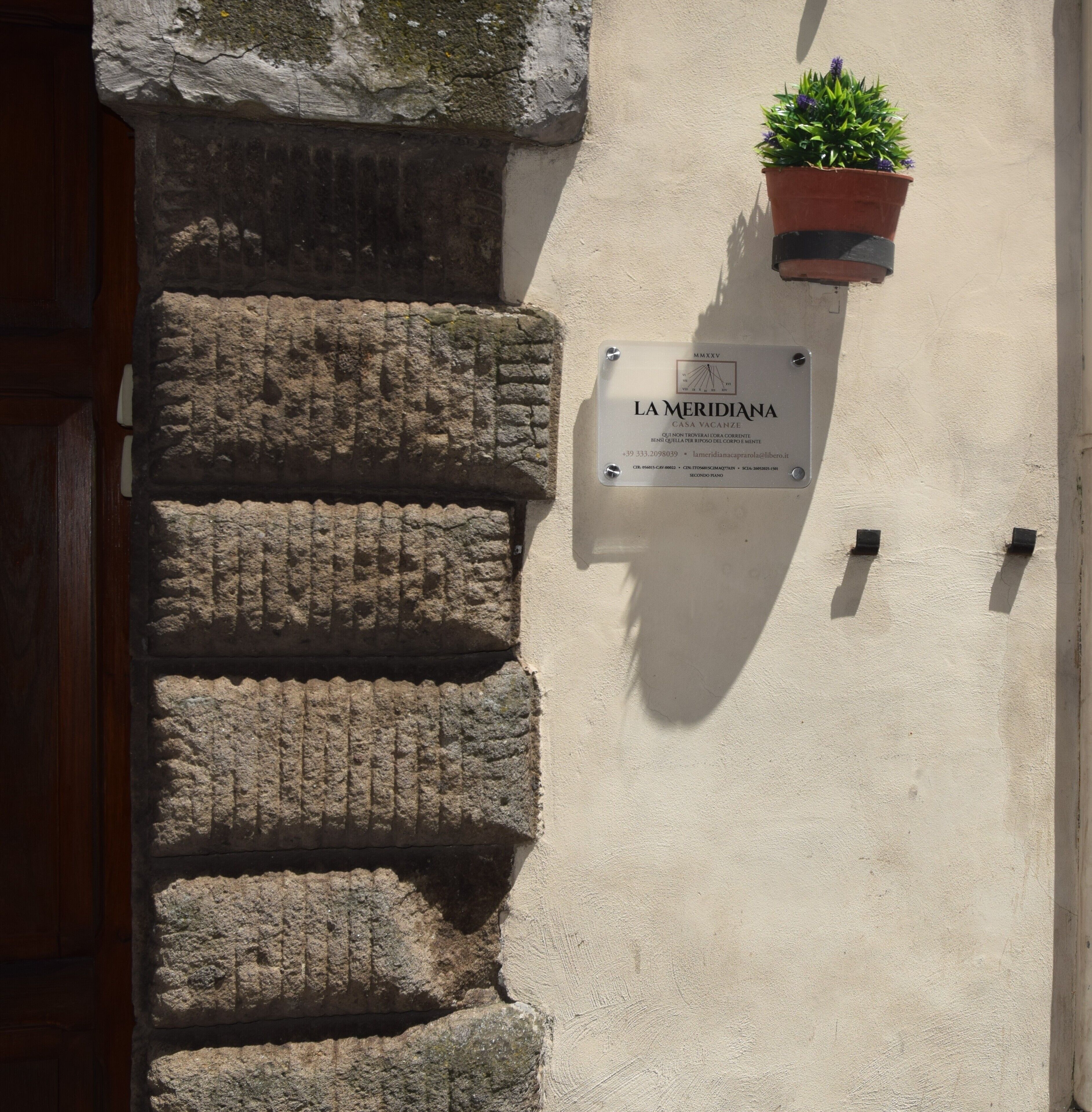 A stone wall with a plaque reading 'LA MERIDIANA' and a potted plant.