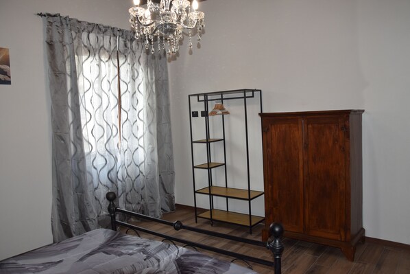 Un dormitorio con una cama, un armario de madera, una estantería metálica y un candelabro.