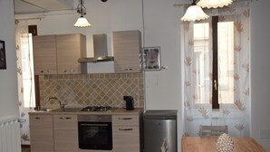 A compact kitchen with wooden cabinets, a built-in oven, a sink, and a compact refrigerator. There is a dining table with a decorative pinecone centerpiece. - In the heart of Caprarola cozy apartment within walking distance of all services (Caprarola)