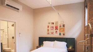 A hotel room with a bed, a headboard, a wall-mounted air conditioner, a ceiling light fixture, and a bathroom visible through an open door. - Toledo Loft | Walk to Ballpark | Suite 204 (Toledo)