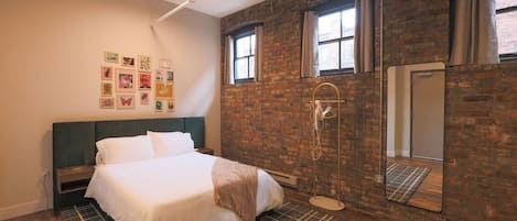 A bedroom with a bed, a wall-mounted mirror, a shower, and a brick wall.
