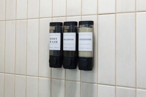 Three toiletries dispensers labeled 'BODY WASH,' 'SHAMPOO,' and 'CONDITIONER' mounted on a tiled wall. - Toledo Loft | Walk to Ballpark | Suite 204 (Toledo)