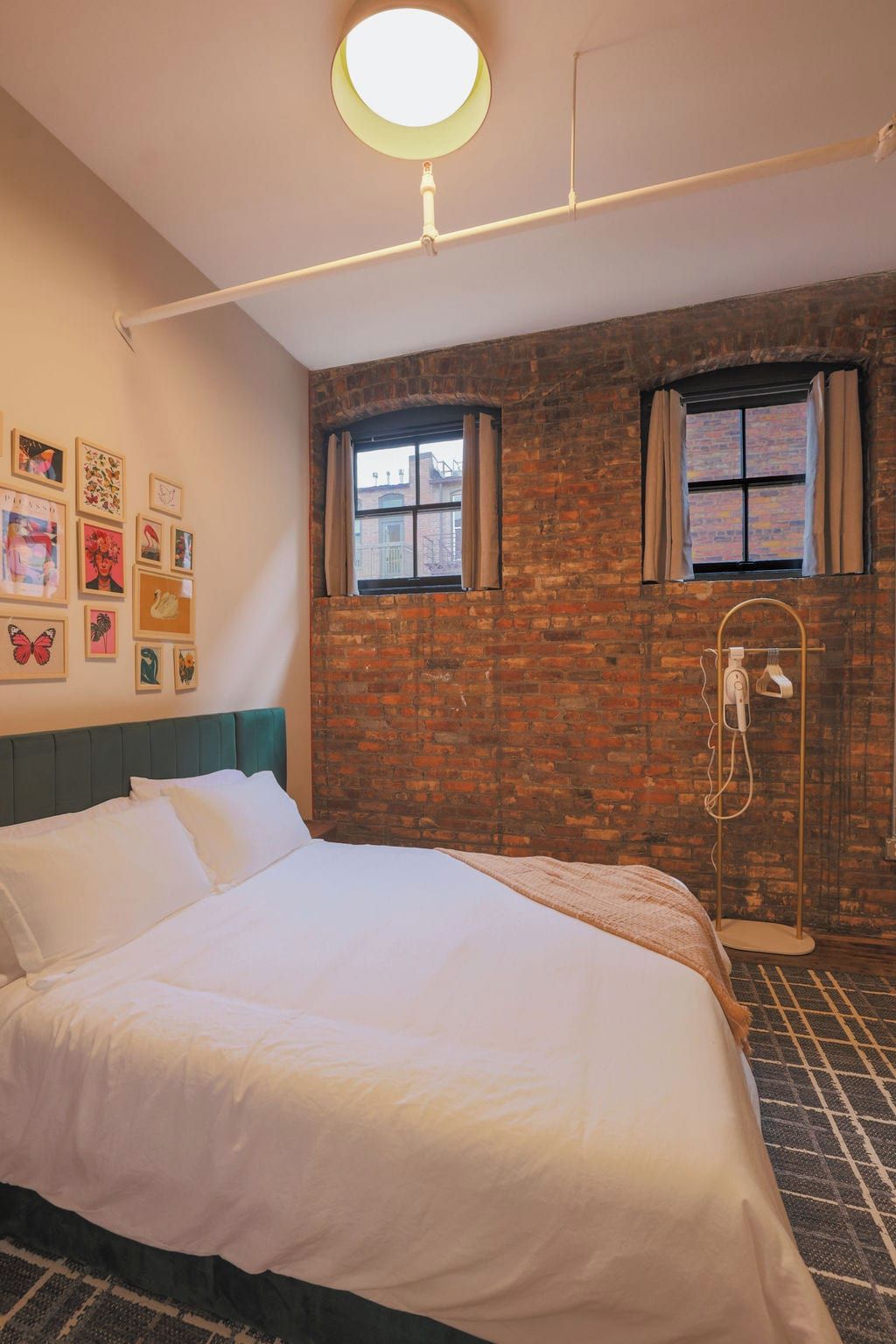 A room with a brick wall, a bed with white bedding, a ceiling light fixture, and a window with curtains.