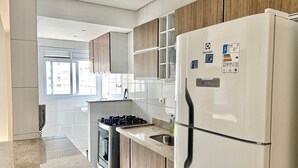 A modern kitchen with a built-in gas stove, a stainless steel refrigerator, and wooden cabinets. - 2 Min da Praia - 2Q - Vaga de Garagem (Santos)