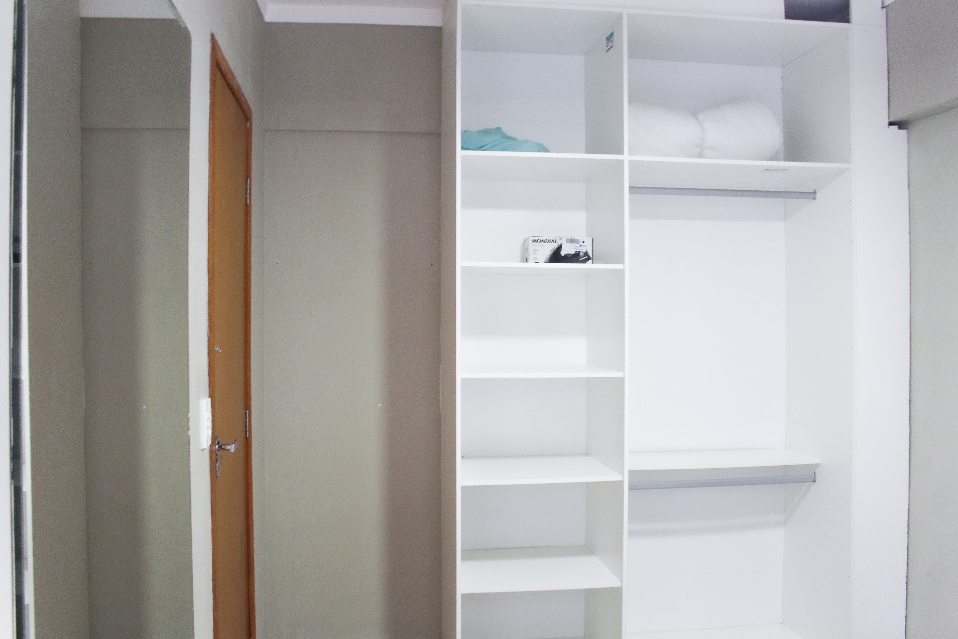 Un armario blanco con varios estantes y espacio para colgar, una puerta de madera y una pared blanca.