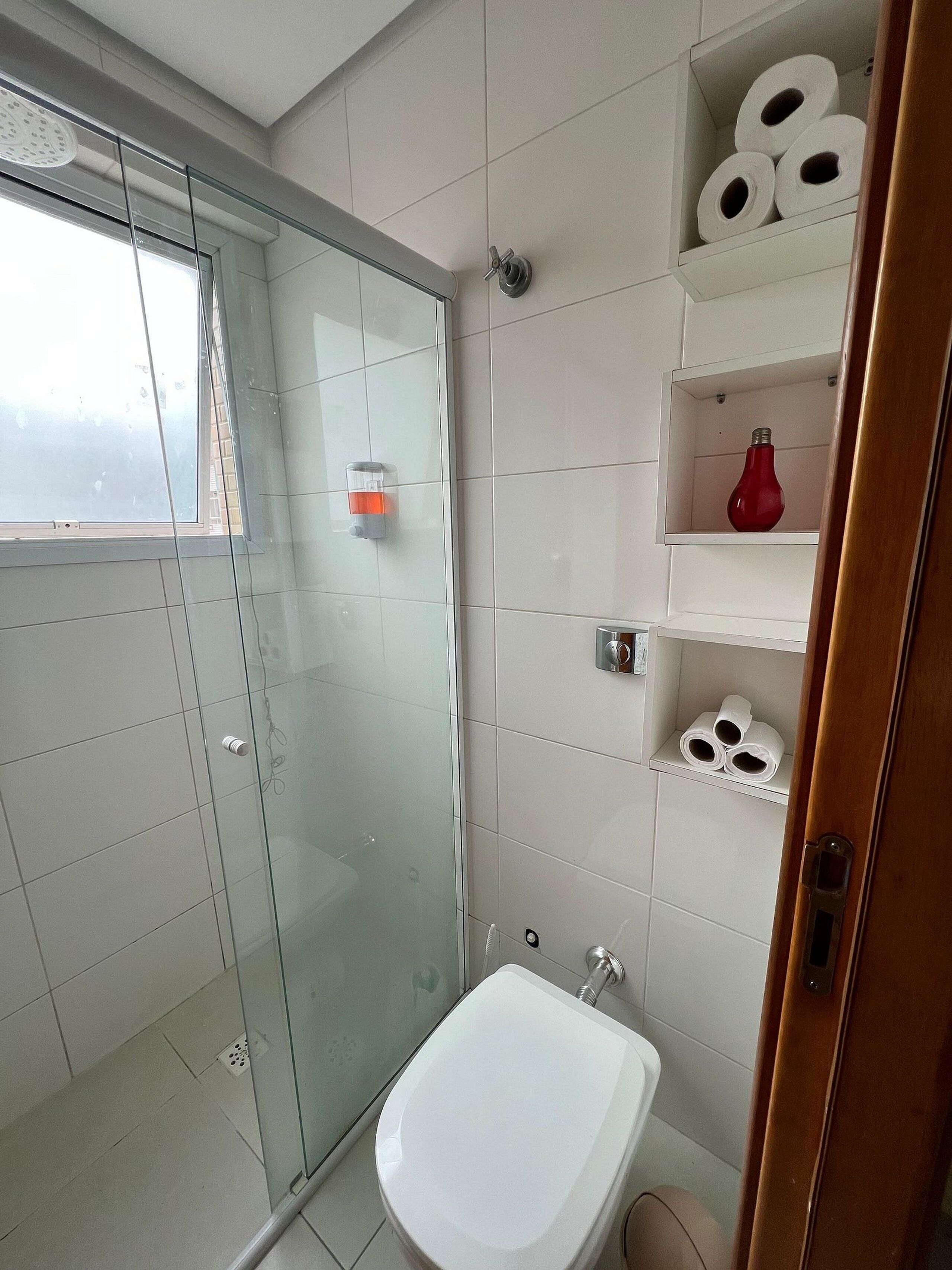 Un baño con cabina de ducha de vidrio, un lavamanos blanco y repisas con artículos de aseo.