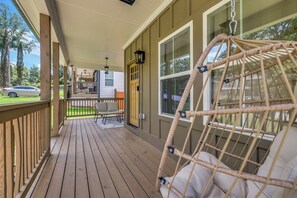 A wooden deck with a wicker swing chair, a covered porch, and a view of a house in the background.