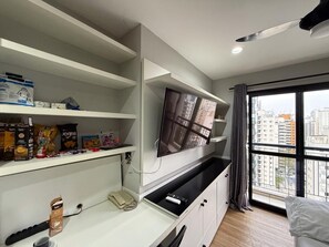 A modern hotel room with a flat-screen TV mounted on the wall, a minibar, and a large window offering a city view. - Private Apartment at the Mercure Hotel - 4-Star Moema SP (Indianópolis São Paulo)