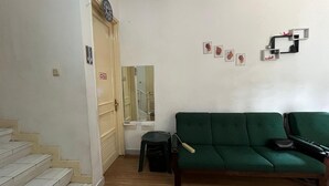 Una sala de estar con un sofá verde, una escalera, una puerta y un reloj fijado a la pared.
