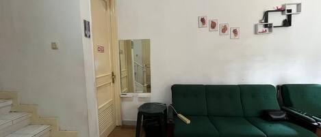 A living room with a green sofa, a staircase, a door, and a wall-mounted clock.
