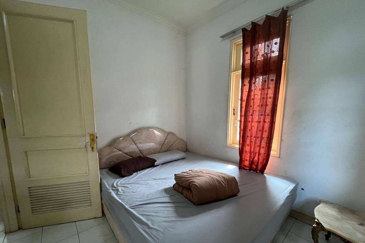 Une chambre à coucher avec un lit, une fenêtre avec des rideaux, une porte et une petite table.