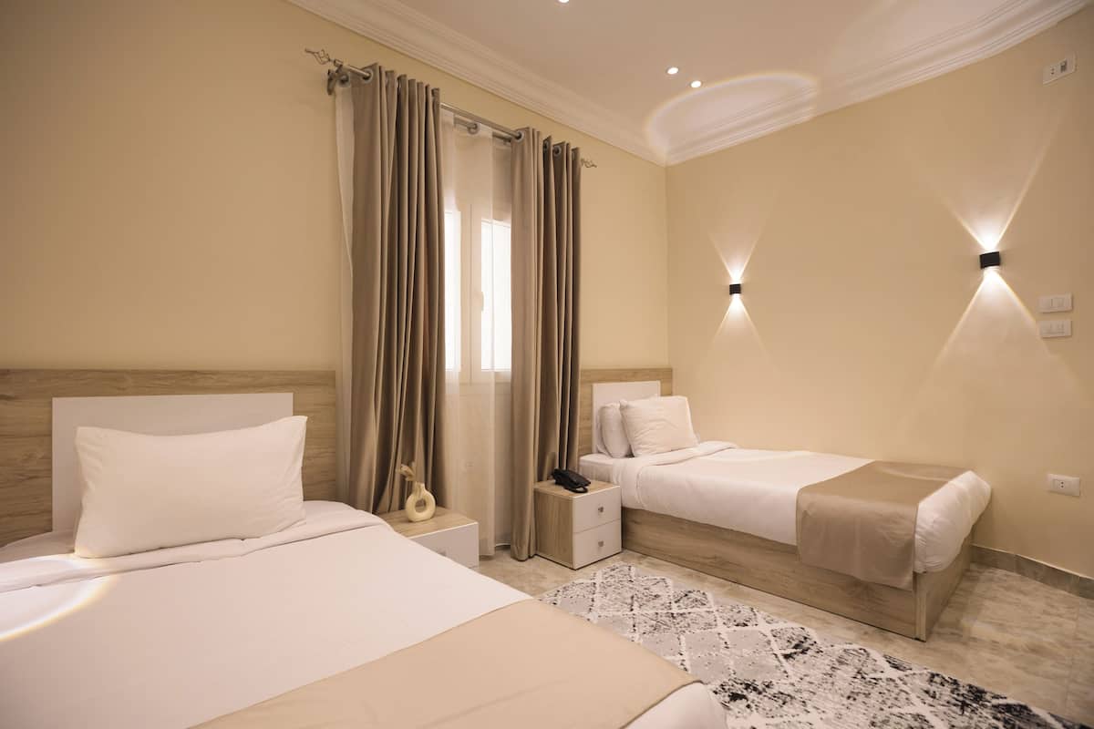 Habitación de hotel con dos camas, una mesita de noche con teléfono, una pequeña mesita auxiliar y una alfombra estampada.