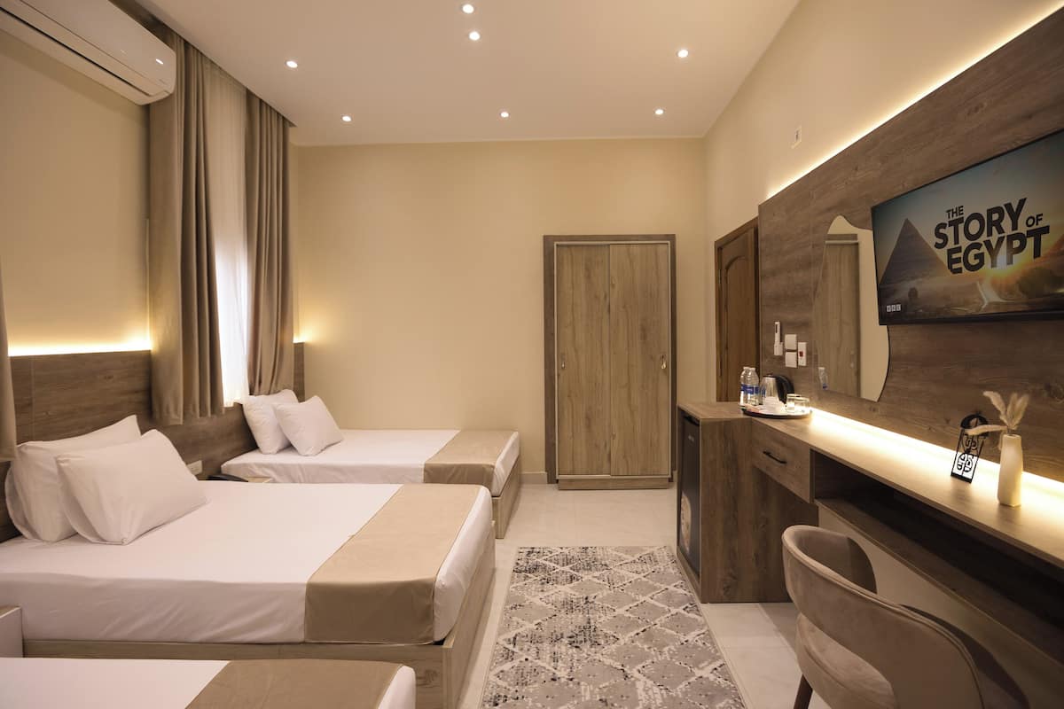 Habitación de hotel con dos camas, un escritorio con televisor, armario y un pequeño rincón de descanso.