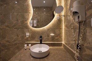 A modern bathroom with a round sink, a mirror, and a hairdryer mounted on the wall. - Secrets Of The Pyramids Hotel (Giza)