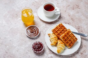 A breakfast setting with waffles, croissants, a cup of coffee, a glass of juice, and a bowl of jam. - Secrets Of The Pyramids Hotel (Giza)