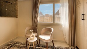 Una habitación moderna con dos sillas, una mesita y vistas a las pirámides a través de una ventana.