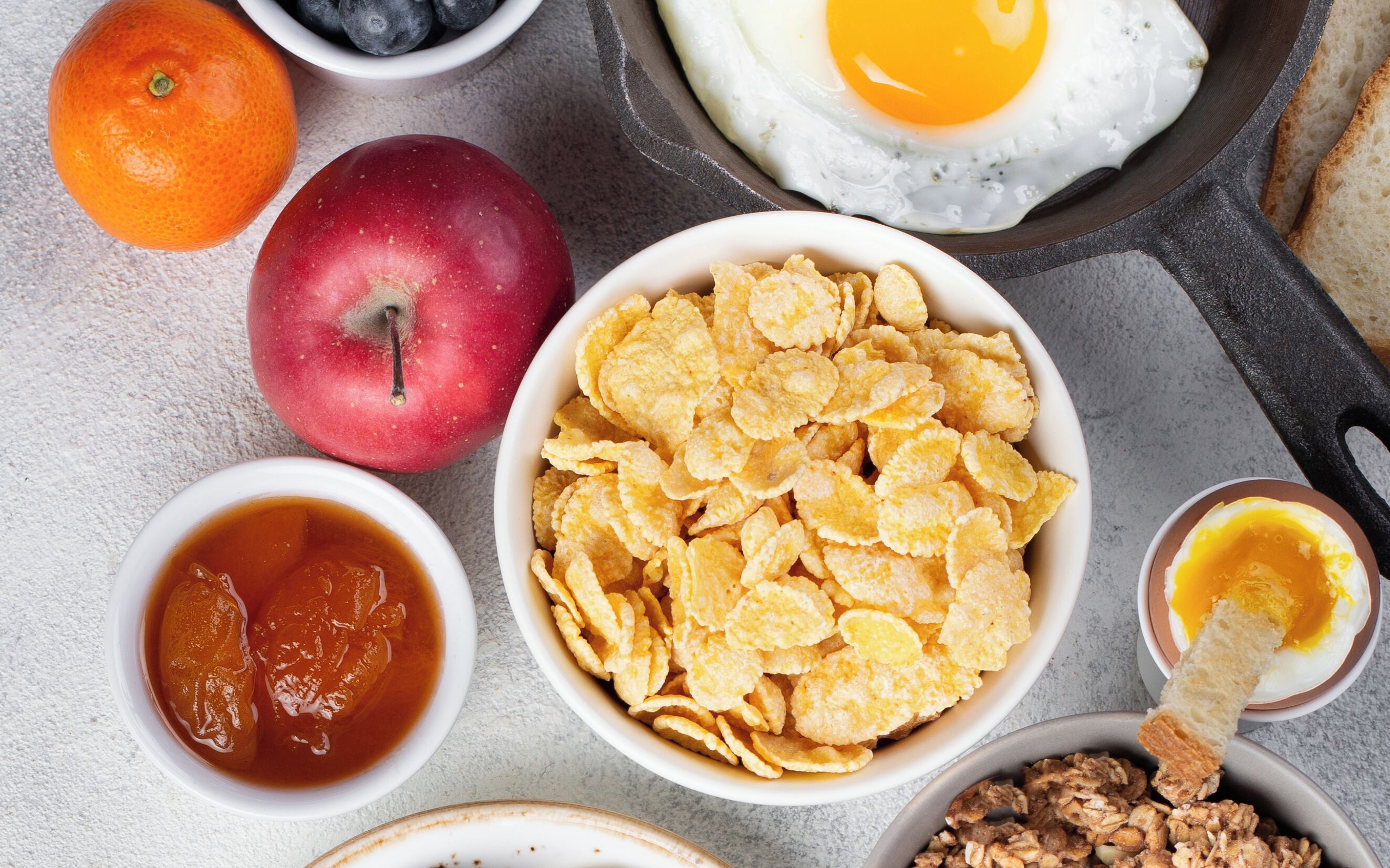 Una mesa con desayuno abundante, incluyendo cereal, huevos, fruta y salsas.