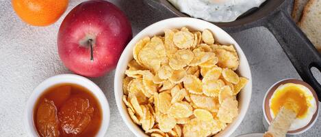 Una mesa con desayuno abundante, incluyendo cereal, huevos, fruta y salsas.
