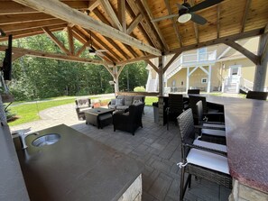 An outdoor patio with a stone countertop, wicker furniture, and a ceiling fan. - Hilltop Haven on Lake Winnisquam (Sanbornton)