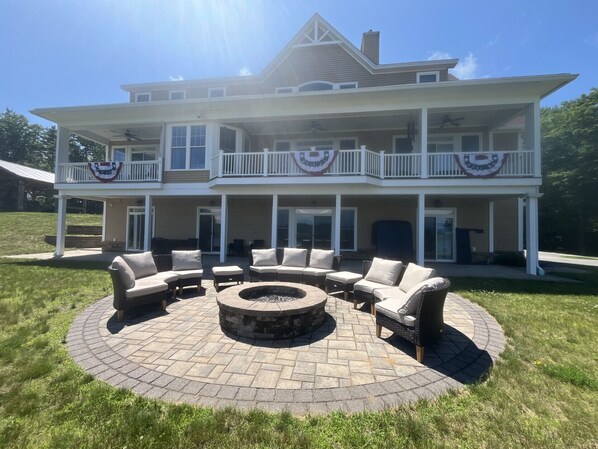 A two-story house with a patio area featuring a circular fire pit and outdoor furniture. - Hilltop Haven on Lake Winnisquam (Sanbornton)