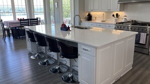 Una cocina amplia con una isla grande, muebles blancos y electrodomésticos de acero inoxidable.