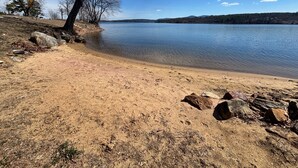 Una playa arenosa con rocas, cielo azul despejado y un lago tranquilo.