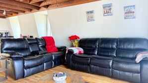 A cozy living room with two black leather sofas, a wooden coffee table, and a mirror reflecting the room. There are three framed signs on the wall, one of which reads "Welcome to the Lake." - Lakeside A-Frame- Cozy Beach Access Retreat (Sanbornton)