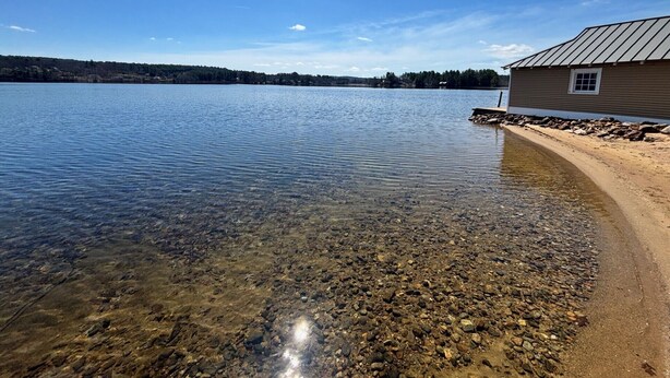 Un chalet au bord du lac offrant une vue dégagée sur l’eau, avec une rive rocheuse et une zone boisée en arrière-plan.