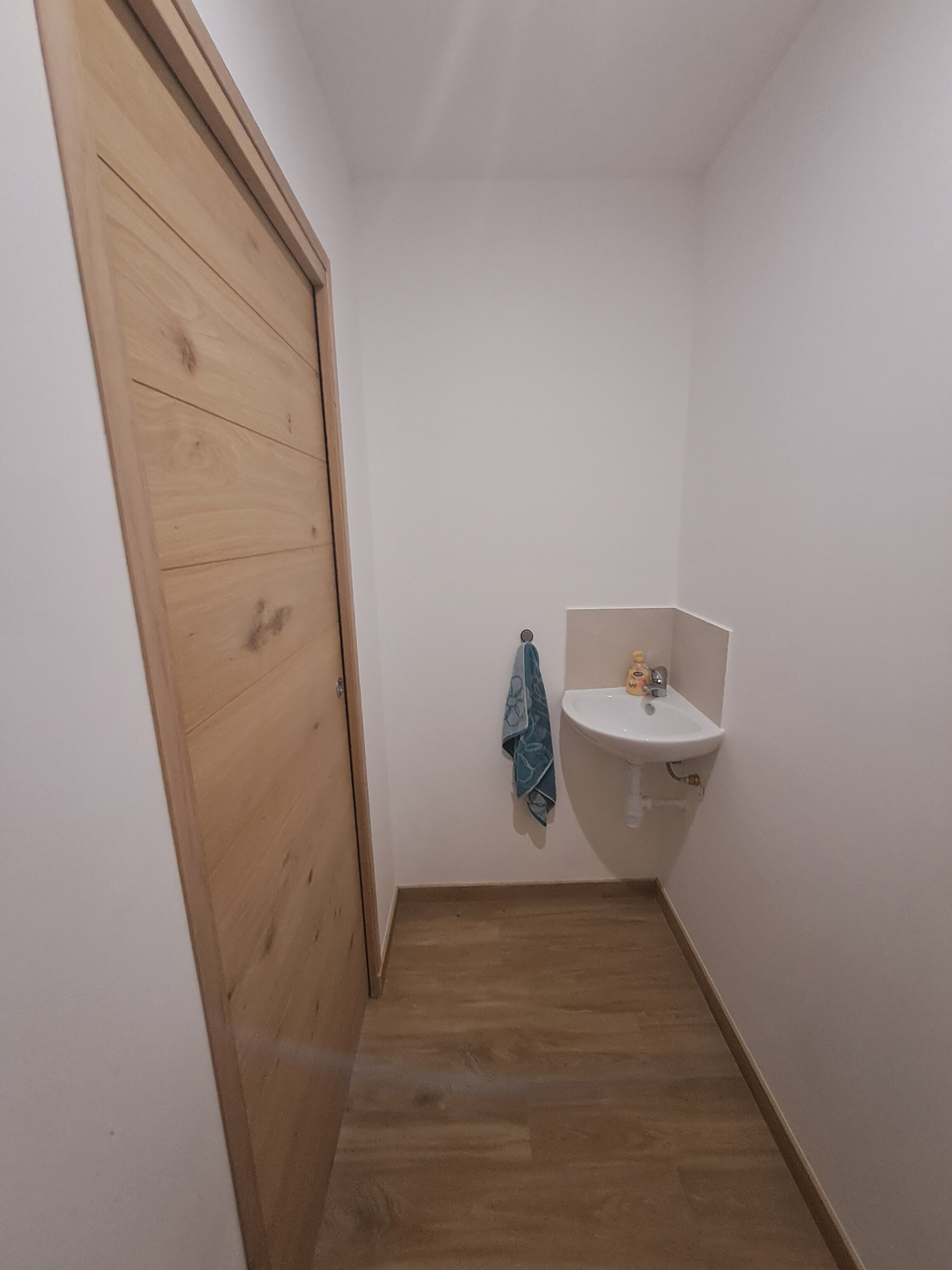 A small bathroom with a wooden door, a white sink, and a blue towel hanging on the wall.