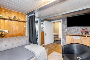 A room with a sofa, a leather chair, a TV, wooden shelves, a stone wall, and a door leading to another room. - Apartment 'Happy 2' with Mountain View, Private Terrace and Wi-Fi (Olsberg)