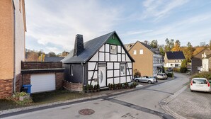 A traditional half-timbered house with a garage, a street with parked cars, and a clear sky. - Apartment 'Happy' with Mountain View, Private Garden and Wi-Fi (Olsberg)