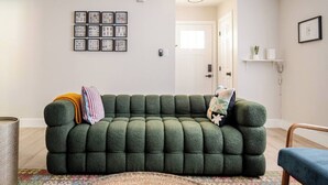 A living room with a green sofa, a patterned rug, and framed pictures on the wall. - Retro Modern Oasis Pool Golf (Las Vegas)