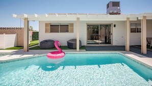 A swimming pool with a pink flamingo float, a covered patio area, and a house with a chimney. - Retro Modern Oasis Pool Golf (Las Vegas)