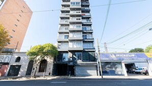 A multi-story building with a garage entrance, a Michelin tire service shop, and a tree in front. - Hornera Caffe - Terminal, Bioceres, IUNIR (Rosario)