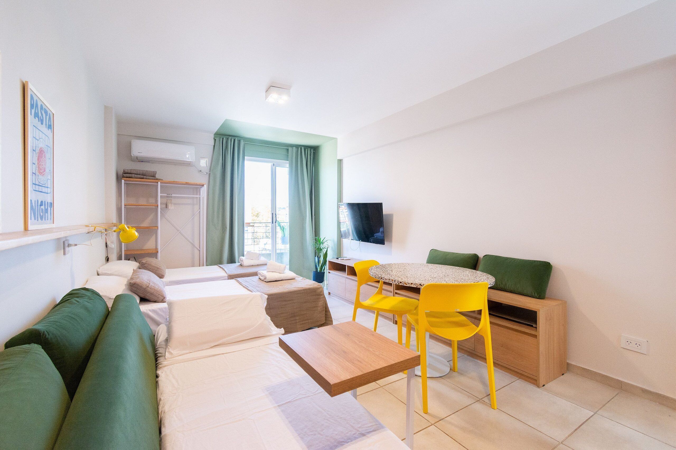 A modern, well-lit room with a bed, a sofa, a dining table with chairs, a TV, and a window with curtains.