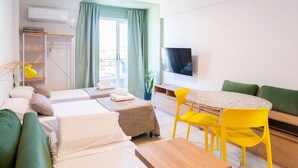 A modern hotel room with two beds, a dining table, yellow chairs, a TV, and a balcony with curtains. - Hornera Caffe - Terminal, Bioceres, IUNIR (Rosario)
