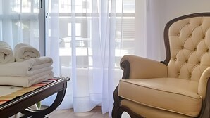 Una habitación con una mesa que sostiene toallas dobladas, un sillón de cuero capitonado y cortinas traslúcidas que dejan entrar luz natural.