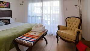 Habitación de hotel con cama, una silla, una mesita con toallas y un cuadro en la pared.