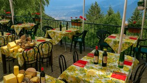 An outdoor dining area with tables covered in floral tablecloths, chairs, and a variety of cheeses and bottles. - Baita Cao Como Lake (Brunate)