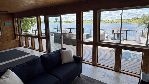 Ein Zimmer mit großem Fenster mit Blick auf einen See, einer Holzzielende und einem dunkelblauen Sofa mit Kissen.