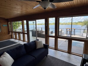 Habitación con un ventanal grande con vistas a un lago, techo de madera y sofá azul oscuro con cojines.