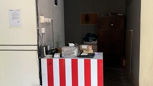 A room with a red and white striped partition, a refrigerator, a desk with a computer, and a door leading to another room.