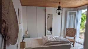 Un dormitorio con cama, una silla, una mesita de noche, una lámpara, un espejo y vistas al exterior.