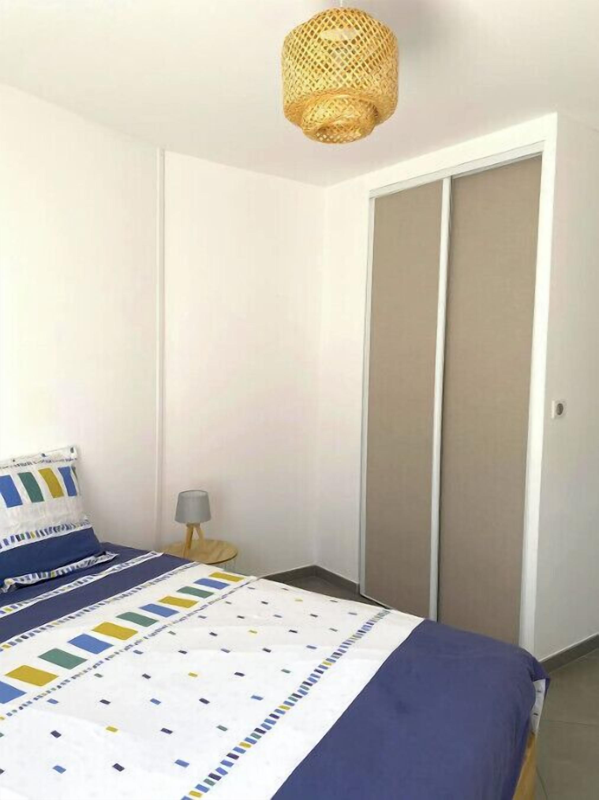 A bedroom with a bed, a nightstand, a lamp, a wardrobe, and a hanging light fixture.