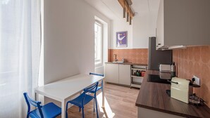 A modern kitchen with a white countertop, a built-in oven, and a coffee machine. There is a window with a view of the street, and a blue chair and table in the dining area. - Apartment in the heart of Marseille, well located (Marseille)