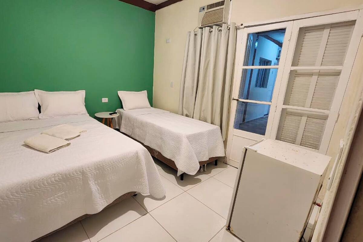Una habitación con dos camas, una pared verde, una ventana con contraventanas y un radiador blanco.