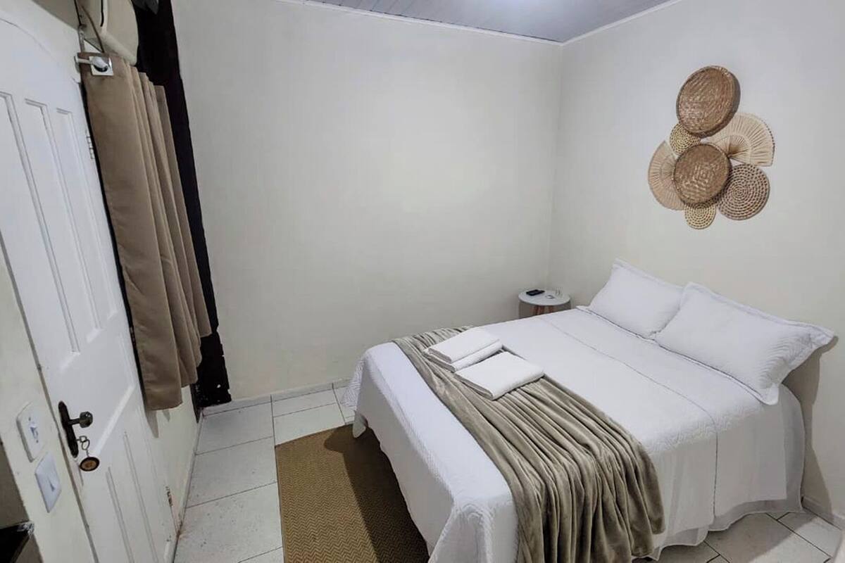 Un dormitorio con cama, mesita de noche, un adorno en la pared y una puerta con una toalla colgada.