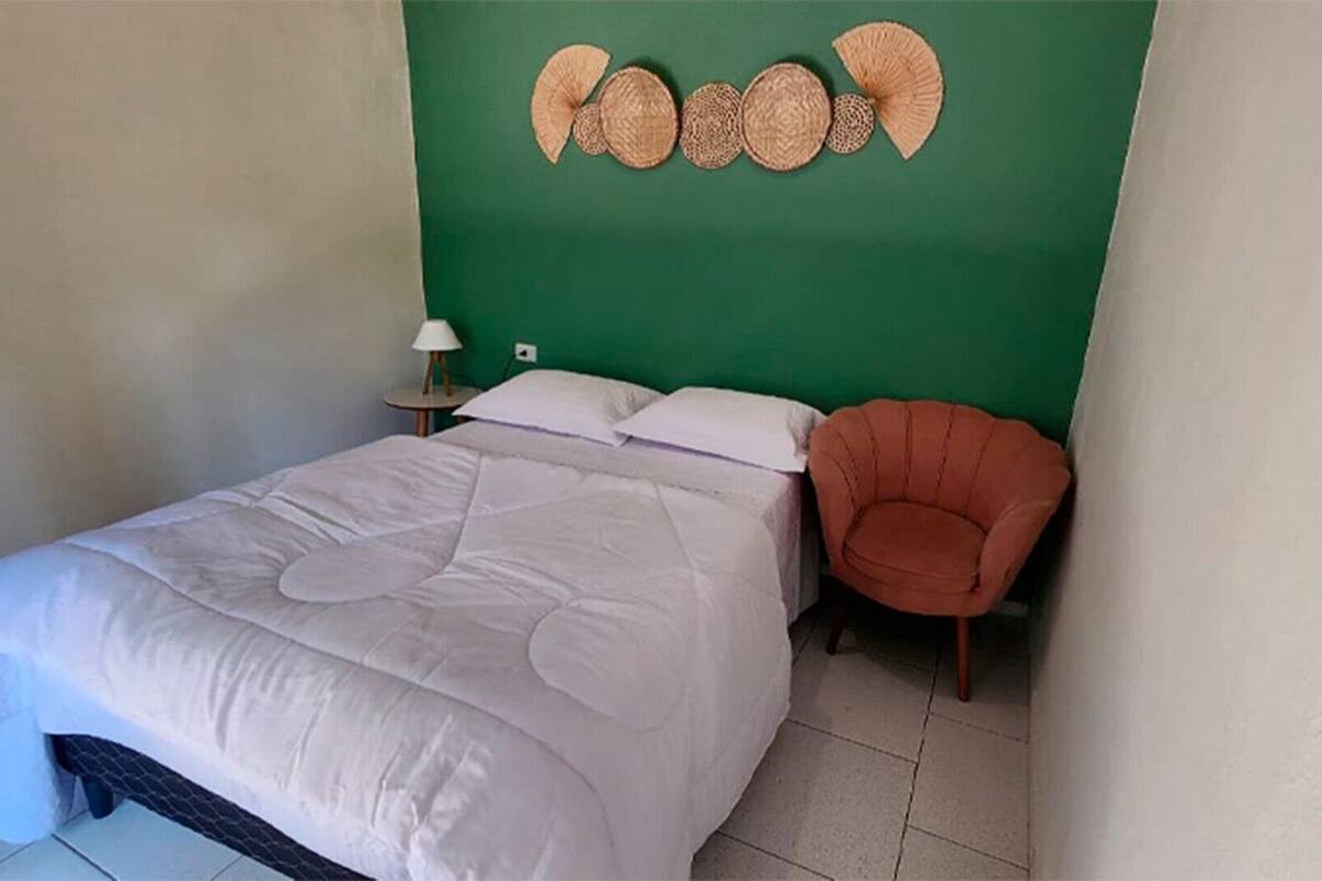 Un dormitorio con cama, mesita de noche, lámpara, silla y pared decorada con tejidos.